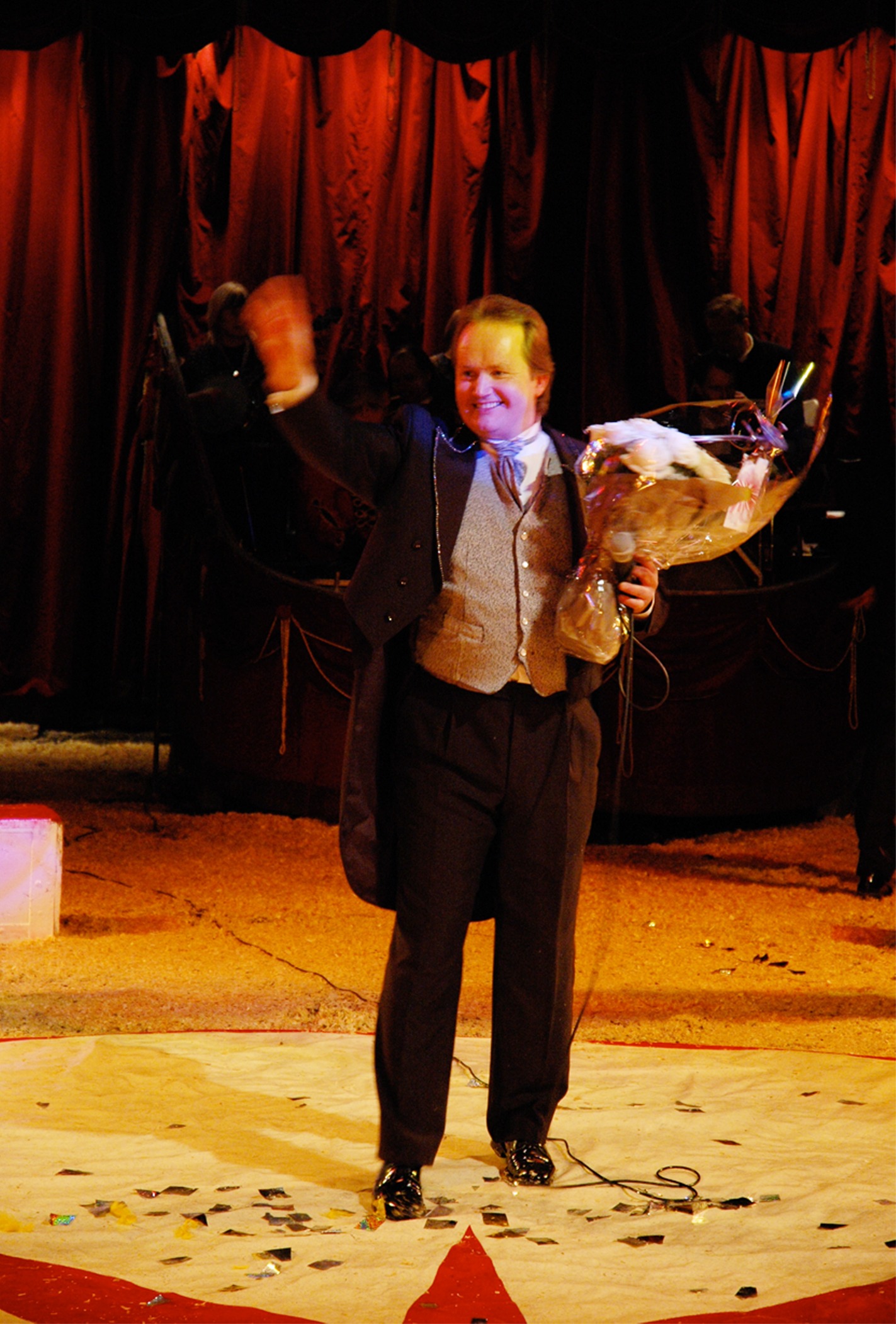 Direktør Smørdal på Agoras første dyrefrie sirkusforestilling står på scenen med blomster og vinker til publikum.